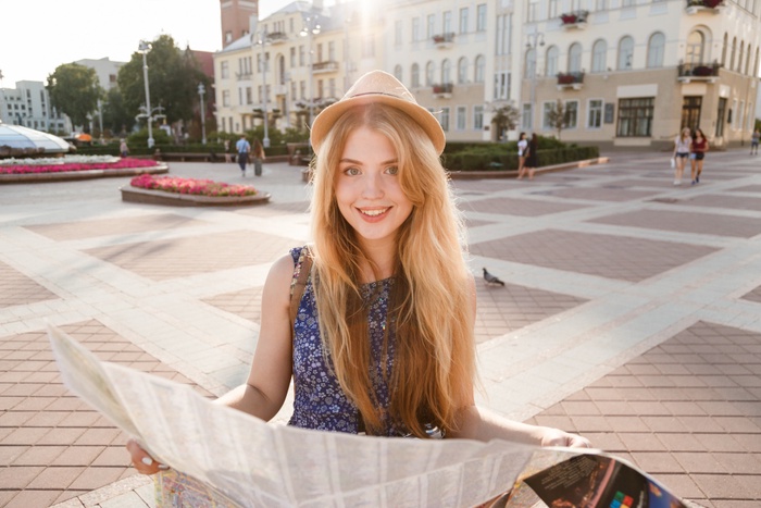 Elegant sugar baby traveler in hat holding map on city street