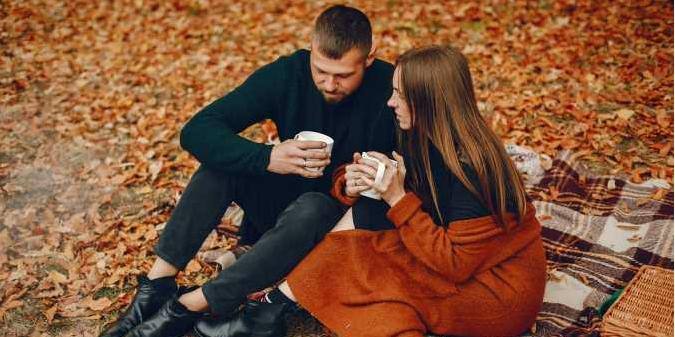 Lovers on autumn leaves, sipping warm drinks.